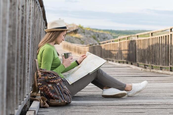 Jeune voyageuse assise sur un pont, consultant une carte pendant un séjour à l’étranger avec un petit budget